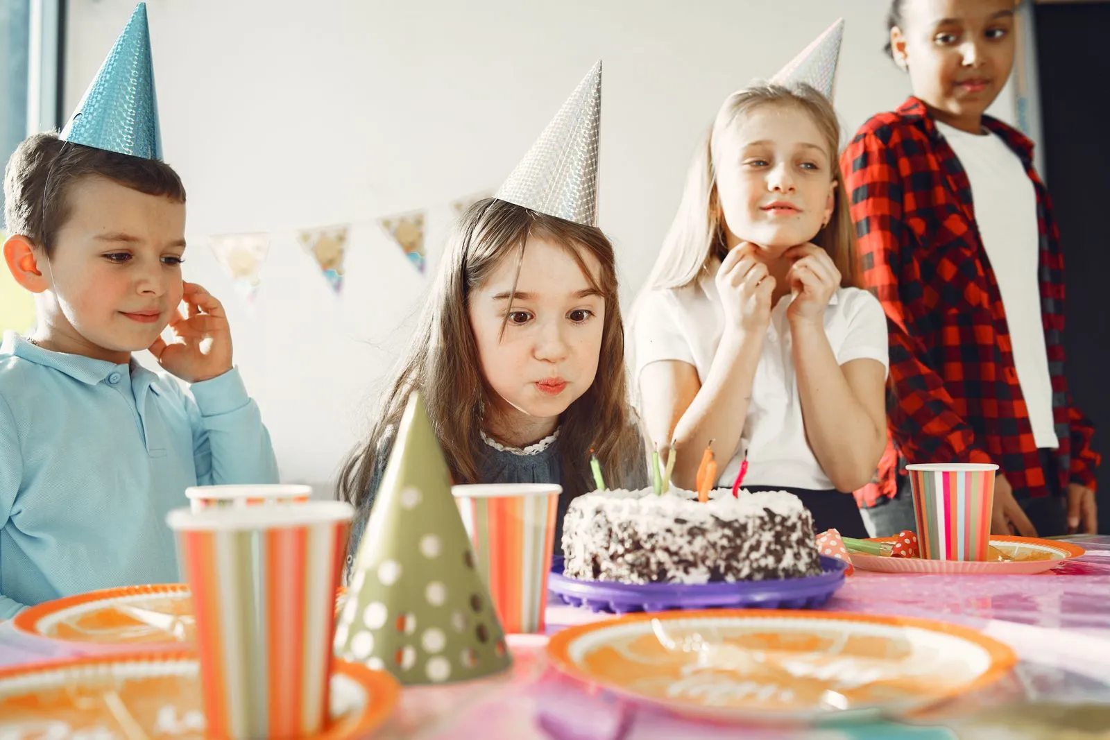 Children celebrating a birthday with cake and party hats indoors. Joyful and festive atmosphere.